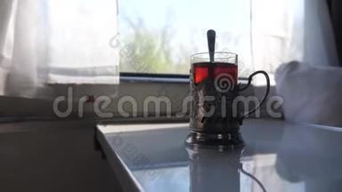铁路旅行概念。 一杯玻璃杯中装有勺子的茶，一个老式的站在火车车厢的桌子上